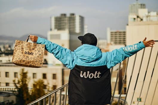 A Wolt courier on a Tel Aviv rooftop, arms open, holding a Wolt bag