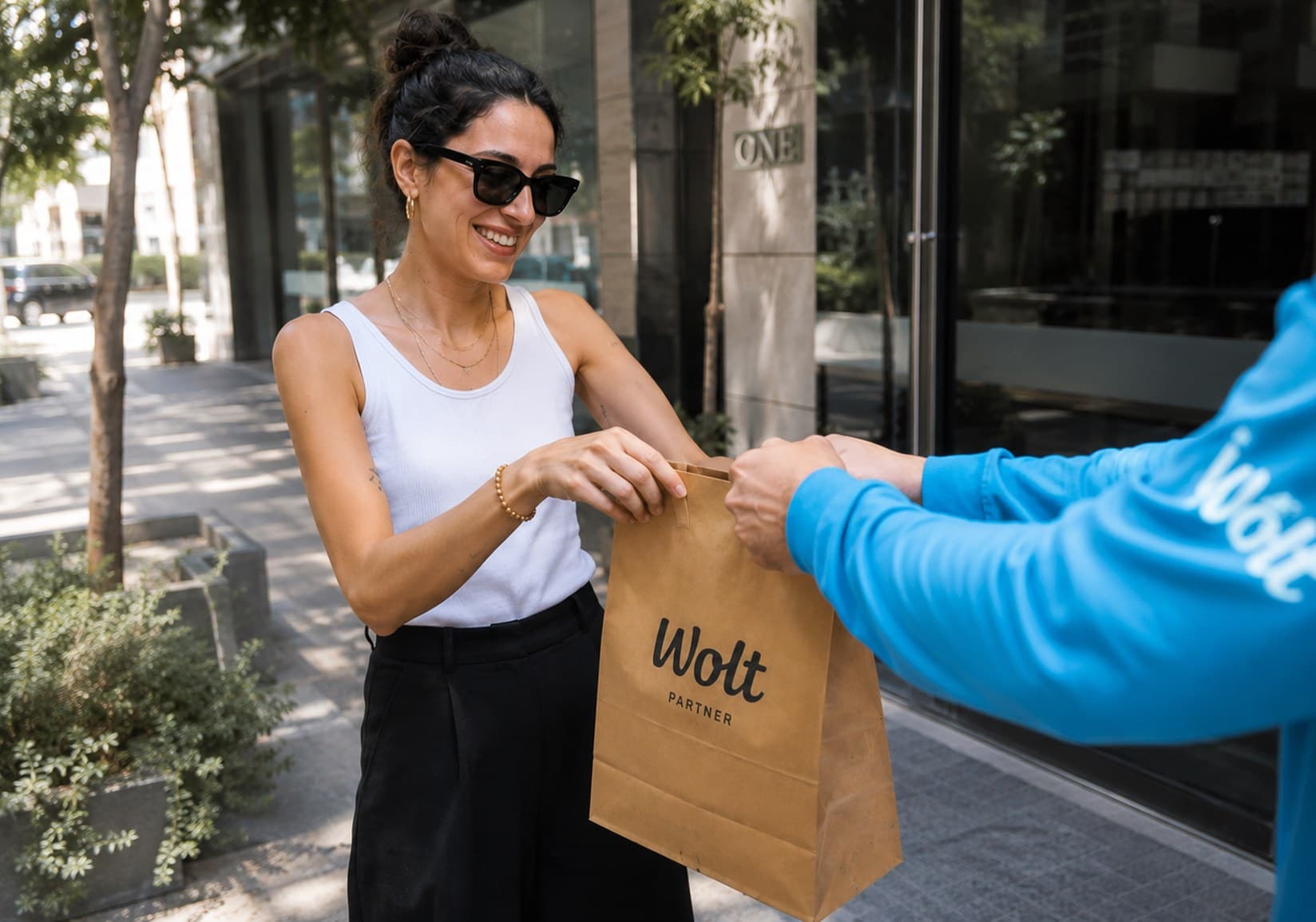 A Wolt courier handing a paper bag to a customer on the street