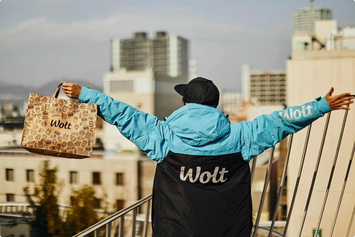 A Wolt courier on a Tel Aviv rooftop, arms open, holding a Wolt bag